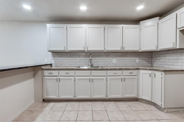 kitchen featuring backsplash, dark stone counters, sink, and white cabinets