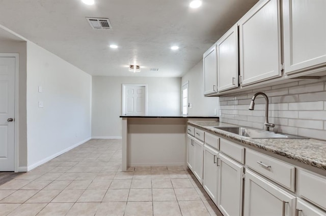 kitchen with tasteful backsplash, white cabinetry, sink, light tile patterned floors, and light stone countertops