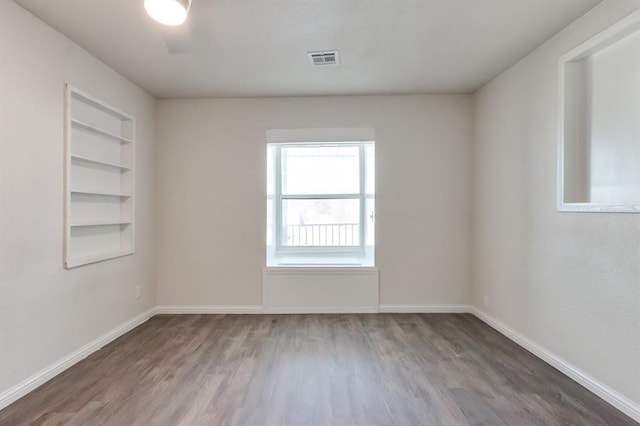 unfurnished room featuring built in shelves and hardwood / wood-style floors