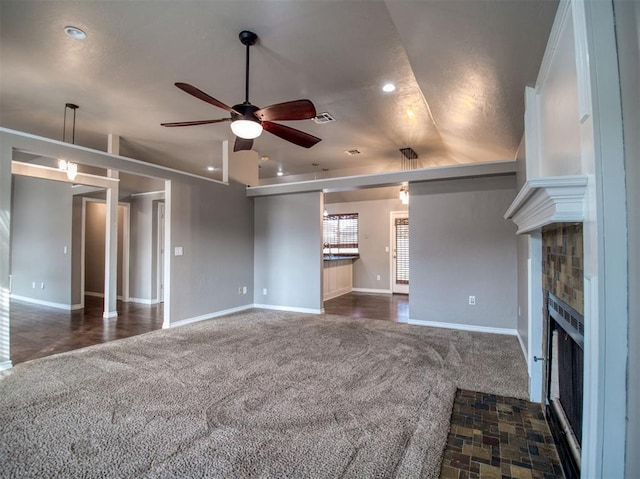 unfurnished living room with dark carpet, a fireplace, and ceiling fan