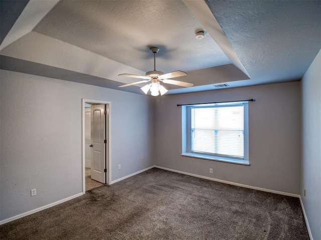 empty room with a raised ceiling, ceiling fan, and carpet