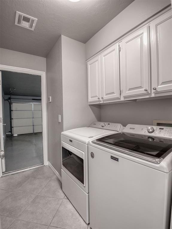 laundry room featuring a textured ceiling, cabinets, light tile patterned flooring, and washer and clothes dryer