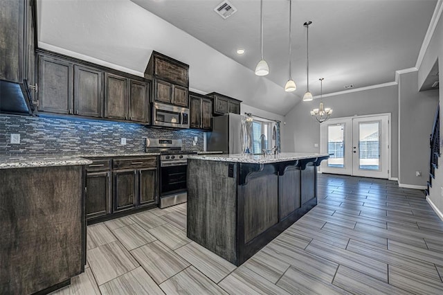 kitchen with appliances with stainless steel finishes, lofted ceiling, french doors, a kitchen breakfast bar, and a kitchen island with sink