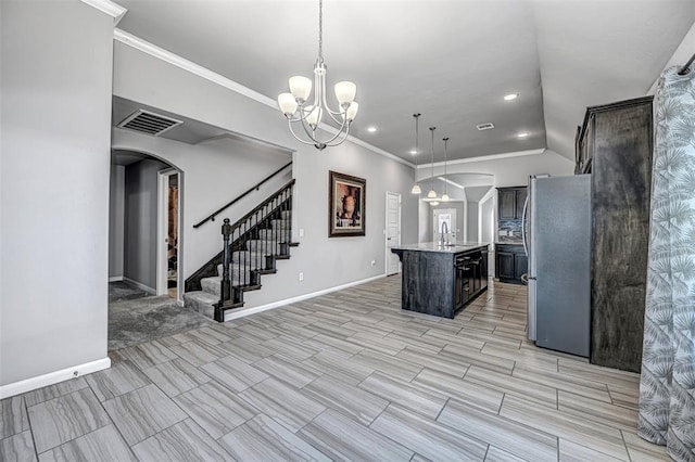 kitchen featuring a notable chandelier, a kitchen island with sink, stainless steel refrigerator, pendant lighting, and sink