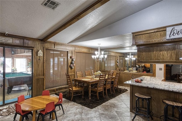 dining space featuring vaulted ceiling with beams, a textured ceiling, wooden walls, and a chandelier