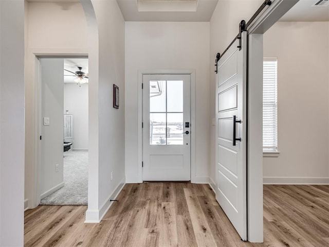 doorway featuring ceiling fan, light hardwood / wood-style floors, a barn door, and a wealth of natural light