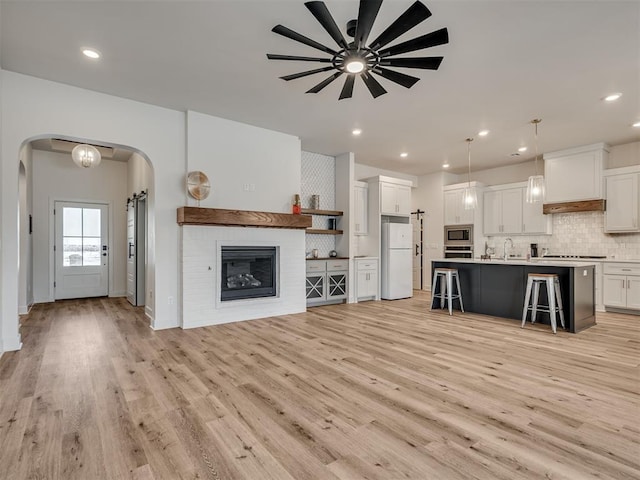 unfurnished living room featuring a fireplace, light hardwood / wood-style flooring, ceiling fan, and sink