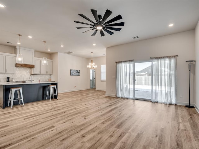 unfurnished living room featuring ceiling fan with notable chandelier and light wood-type flooring