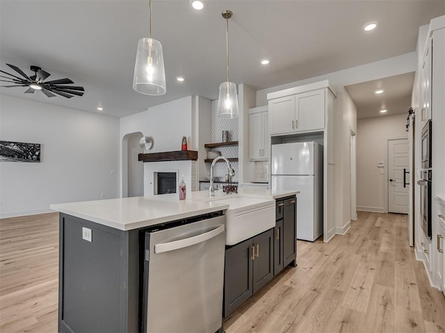 kitchen featuring a kitchen island with sink, white cabinets, sink, appliances with stainless steel finishes, and decorative light fixtures