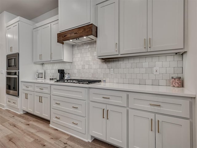 kitchen with stainless steel appliances, tasteful backsplash, light hardwood / wood-style floors, white cabinets, and custom range hood