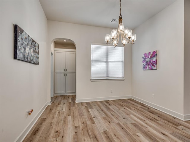 spare room featuring light wood-type flooring and a notable chandelier