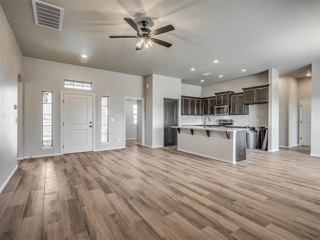 kitchen with ceiling fan, sink, stainless steel appliances, a kitchen island with sink, and a breakfast bar