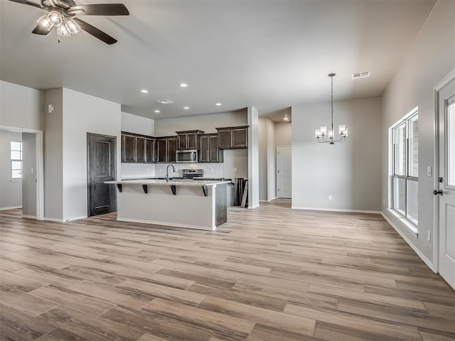 kitchen with dark brown cabinetry, stainless steel appliances, light hardwood / wood-style floors, decorative light fixtures, and ceiling fan with notable chandelier