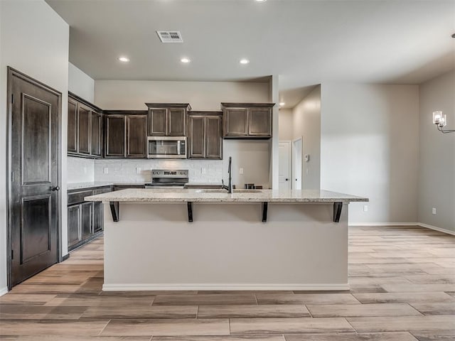 kitchen featuring light stone countertops, sink, a kitchen breakfast bar, an island with sink, and appliances with stainless steel finishes