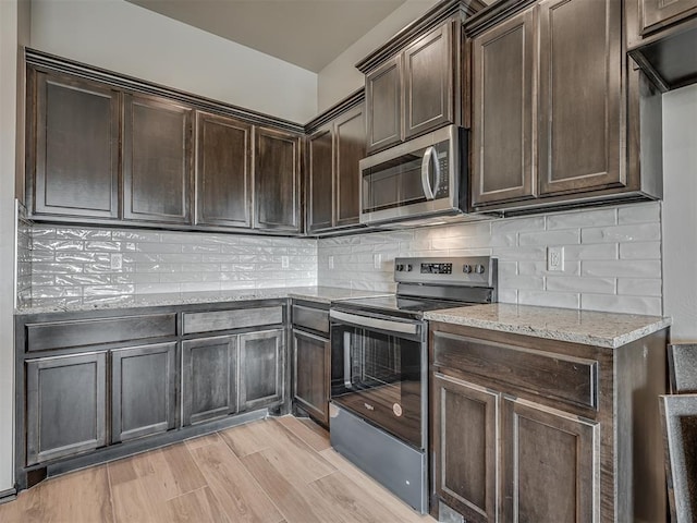 kitchen featuring decorative backsplash, light stone counters, dark brown cabinetry, and stainless steel appliances