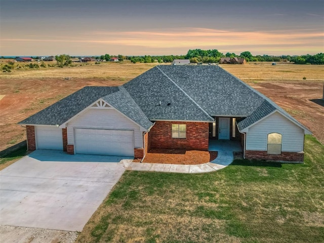 view of front of house with roof with shingles, driveway, an attached garage, a yard, and brick siding