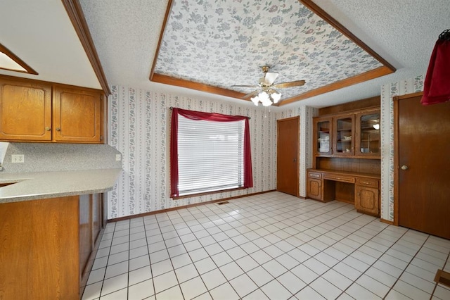 kitchen featuring built in desk, a raised ceiling, ceiling fan, and light tile patterned flooring