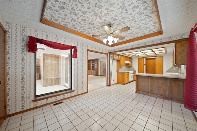 kitchen featuring ceiling fan, light tile patterned floors, kitchen peninsula, white range with electric stovetop, and a tray ceiling