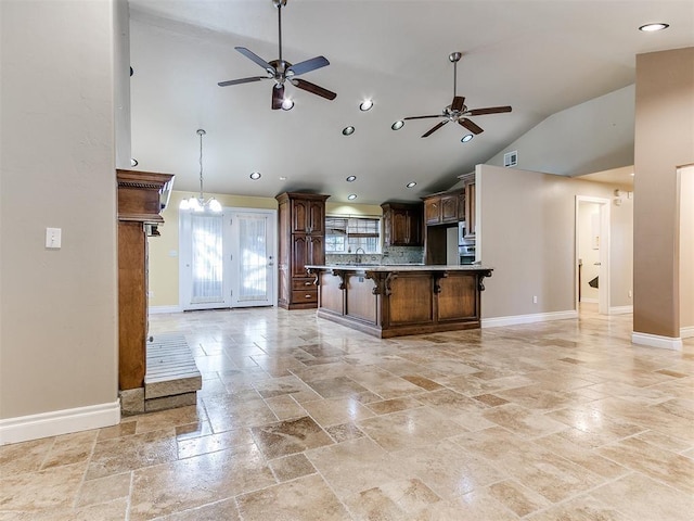 kitchen with sink, vaulted ceiling, a kitchen bar, ceiling fan with notable chandelier, and hanging light fixtures