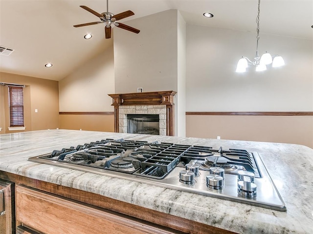 kitchen featuring stainless steel gas stovetop, pendant lighting, a fireplace, lofted ceiling, and ceiling fan with notable chandelier