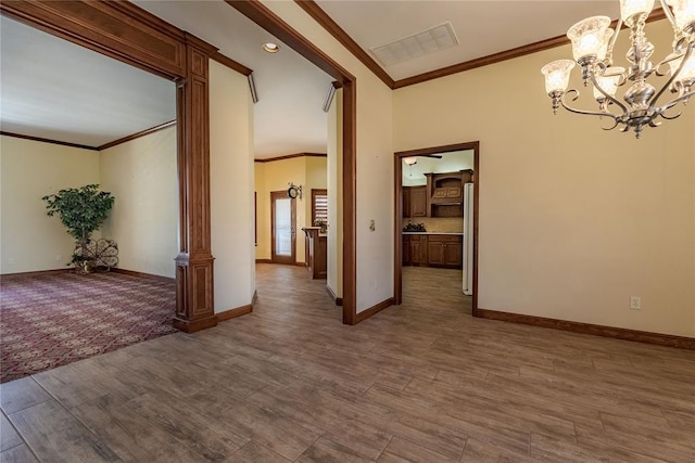 empty room featuring a notable chandelier, hardwood / wood-style flooring, ornamental molding, and ornate columns