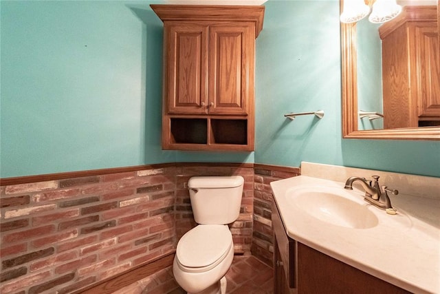 bathroom with vanity, toilet, and brick wall