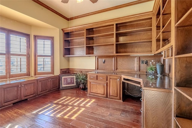 unfurnished office featuring built in desk, dark wood-type flooring, ornamental molding, and ceiling fan