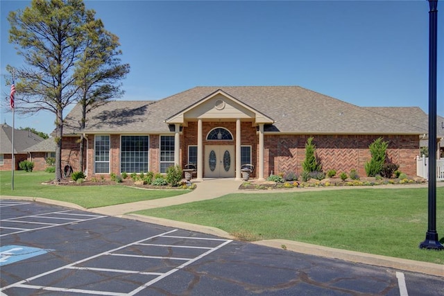 view of front of home featuring roof with shingles, a front yard, uncovered parking, and brick siding