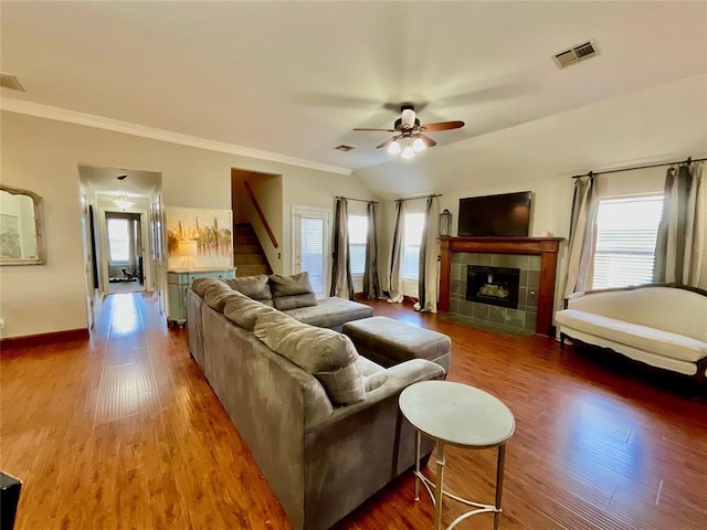 living room featuring ceiling fan, dark wood-type flooring, vaulted ceiling, a tiled fireplace, and ornamental molding