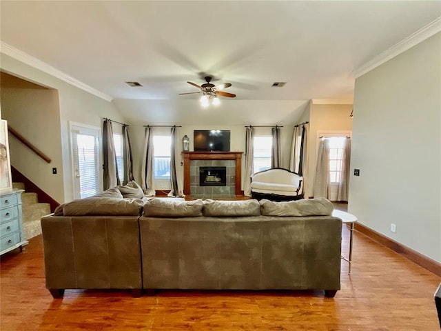 living room with crown molding, vaulted ceiling, hardwood / wood-style flooring, ceiling fan, and a tiled fireplace