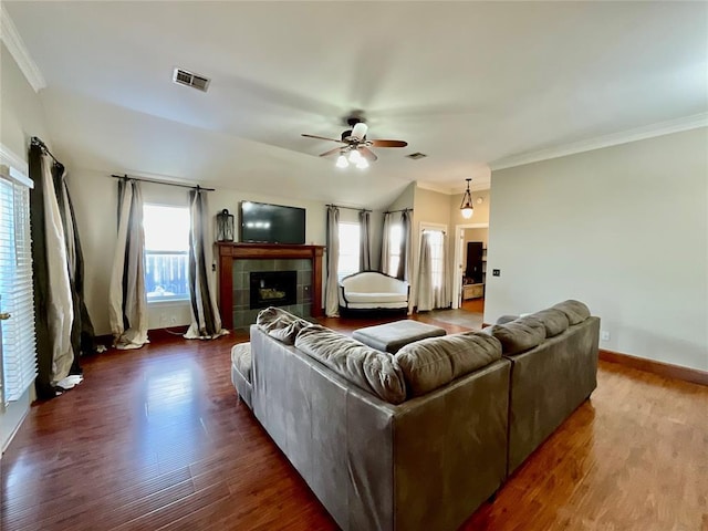 living room featuring ceiling fan, dark wood-type flooring, vaulted ceiling, a tiled fireplace, and ornamental molding