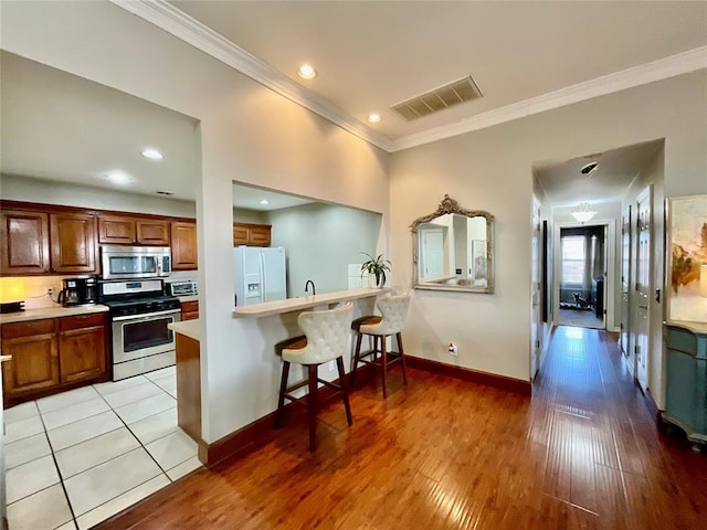 kitchen featuring kitchen peninsula, appliances with stainless steel finishes, a breakfast bar area, light tile patterned floors, and ornamental molding