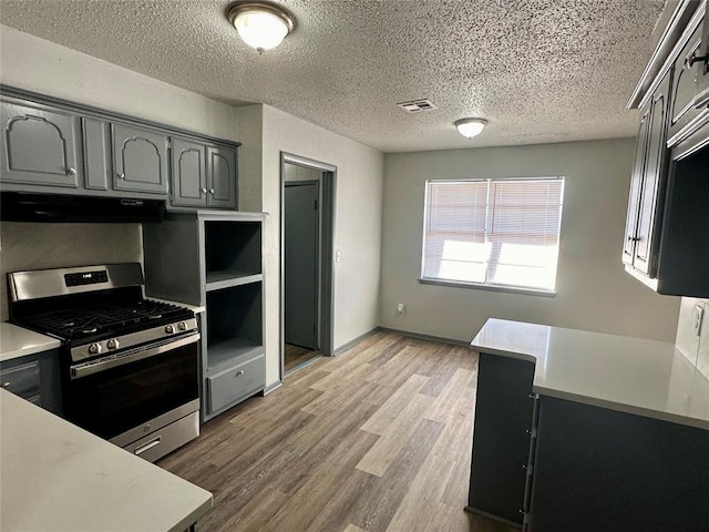 kitchen with a textured ceiling, gas stove, gray cabinetry, and hardwood / wood-style floors