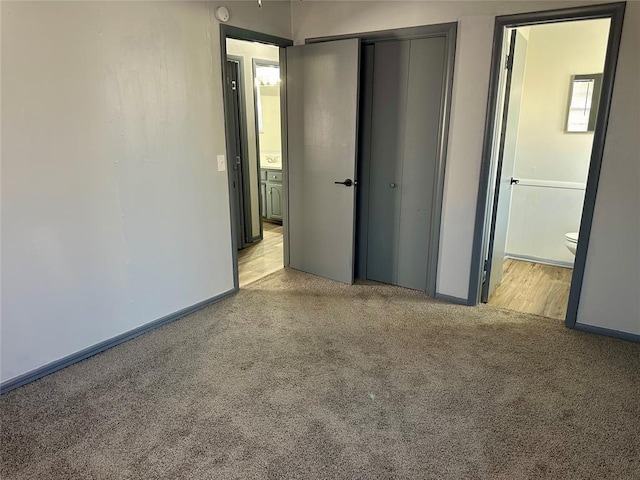 unfurnished bedroom featuring a closet, ensuite bathroom, and light colored carpet