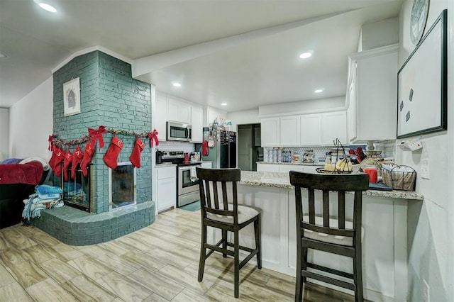 kitchen featuring a kitchen bar, appliances with stainless steel finishes, backsplash, and white cabinetry