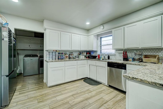 kitchen with appliances with stainless steel finishes, washer and clothes dryer, light stone countertops, white cabinetry, and backsplash