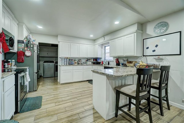 kitchen with light stone countertops, a kitchen bar, washer / dryer, white cabinets, and appliances with stainless steel finishes