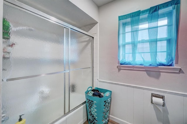 bathroom featuring wood walls and combined bath / shower with glass door