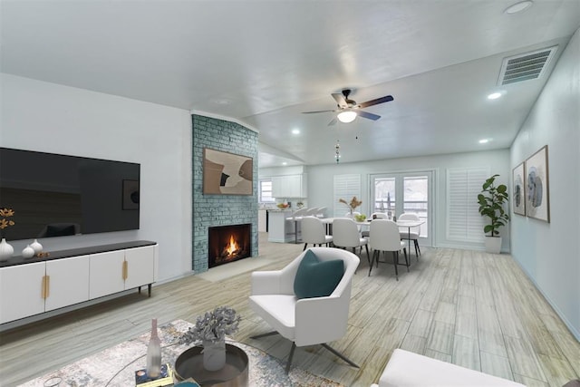 living room featuring vaulted ceiling, a fireplace, ceiling fan, and light hardwood / wood-style floors