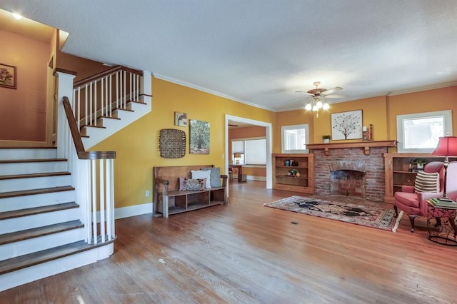 living room featuring hardwood / wood-style flooring, ceiling fan, ornamental molding, and a brick fireplace