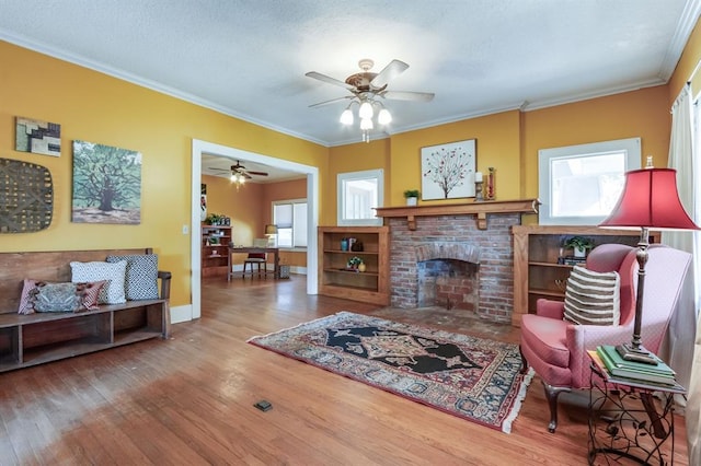 living room featuring a fireplace, hardwood / wood-style floors, ceiling fan, and crown molding