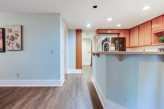 kitchen with a breakfast bar, stainless steel fridge, light wood-type flooring, and kitchen peninsula