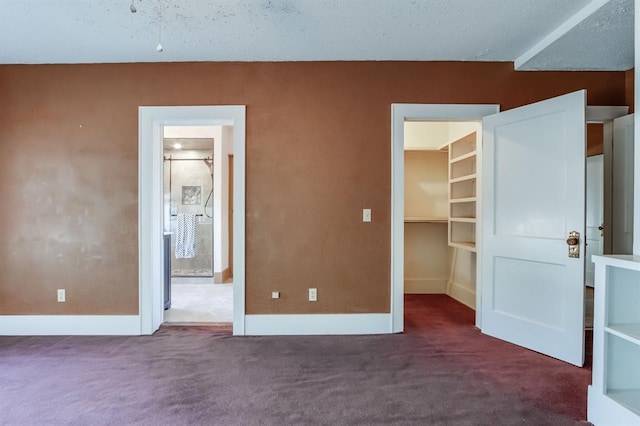 unfurnished bedroom with a textured ceiling, a walk in closet, dark carpet, and ensuite bath