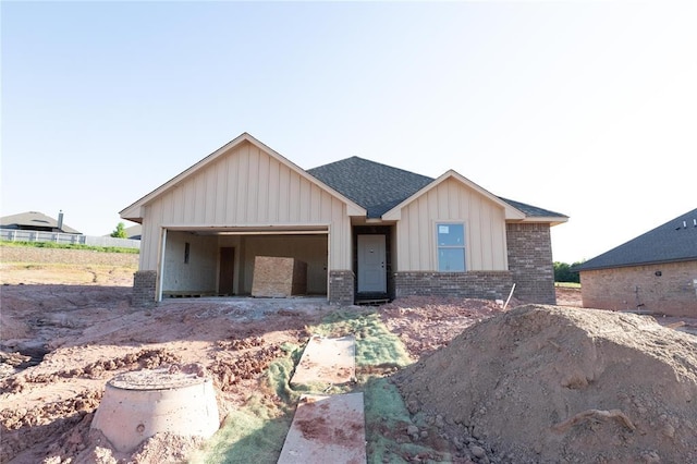view of front facade with board and batten siding, brick siding, an attached garage, a shingled roof, and driveway