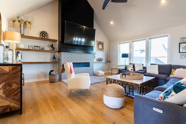 living room with light hardwood / wood-style flooring, a tile fireplace, and high vaulted ceiling