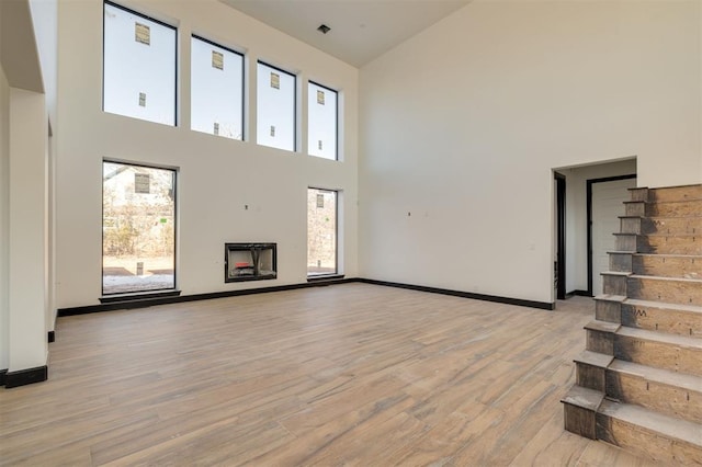 unfurnished living room with a towering ceiling, a fireplace, light wood-type flooring, and a wealth of natural light