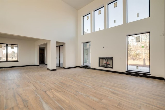 unfurnished living room with a towering ceiling and light wood-type flooring