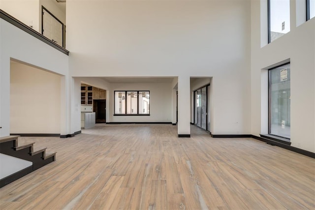 unfurnished living room featuring light hardwood / wood-style floors and a towering ceiling