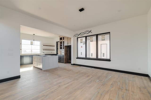 kitchen with decorative light fixtures, light wood-type flooring, a kitchen island, and white cabinetry