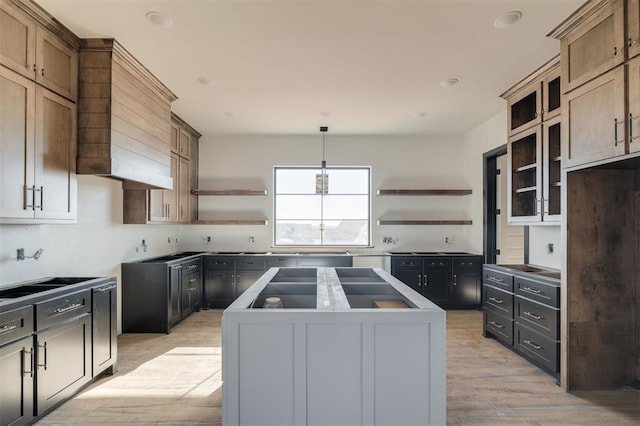 kitchen featuring hanging light fixtures, stovetop, light brown cabinetry, a kitchen island, and light hardwood / wood-style flooring